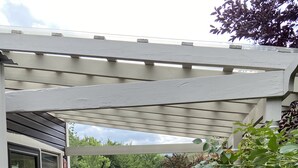 A covered patio with a wooden deck, outdoor furniture, and a pergola.
