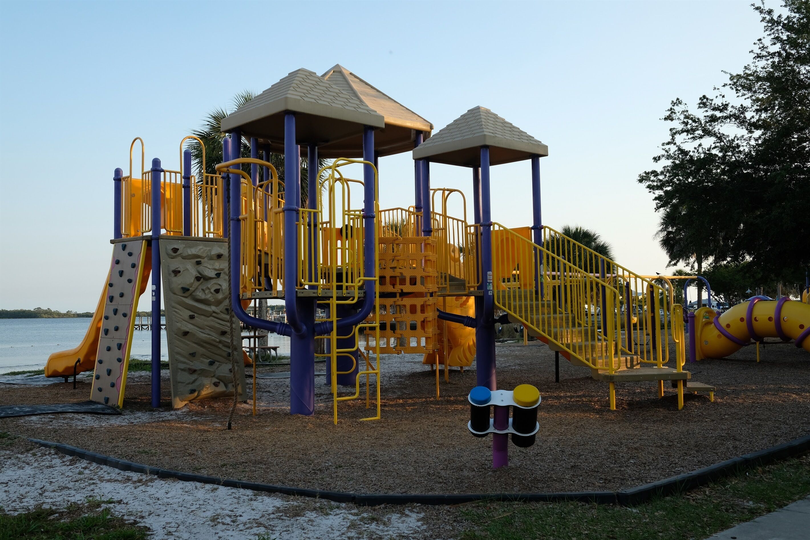 A playground with climbing structures, slides, and a sandy area near water.