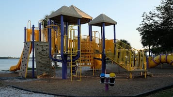 A playground with climbing structures, slides, and a sandy area near water.