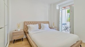 A bedroom with a large bed, a nightstand, and a sliding glass door leading to an outdoor area. - Garrett Terrace (Setúbal)