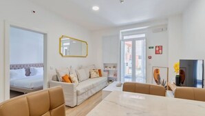 A modern hotel room with a bed, a sofa, a dining table, and a TV. - Garrett Terrace (Setúbal)