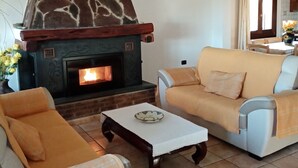 A living room with a fireplace, two sofas, a coffee table, and a hanging light fixture. - Villa Lupino (Orosei)