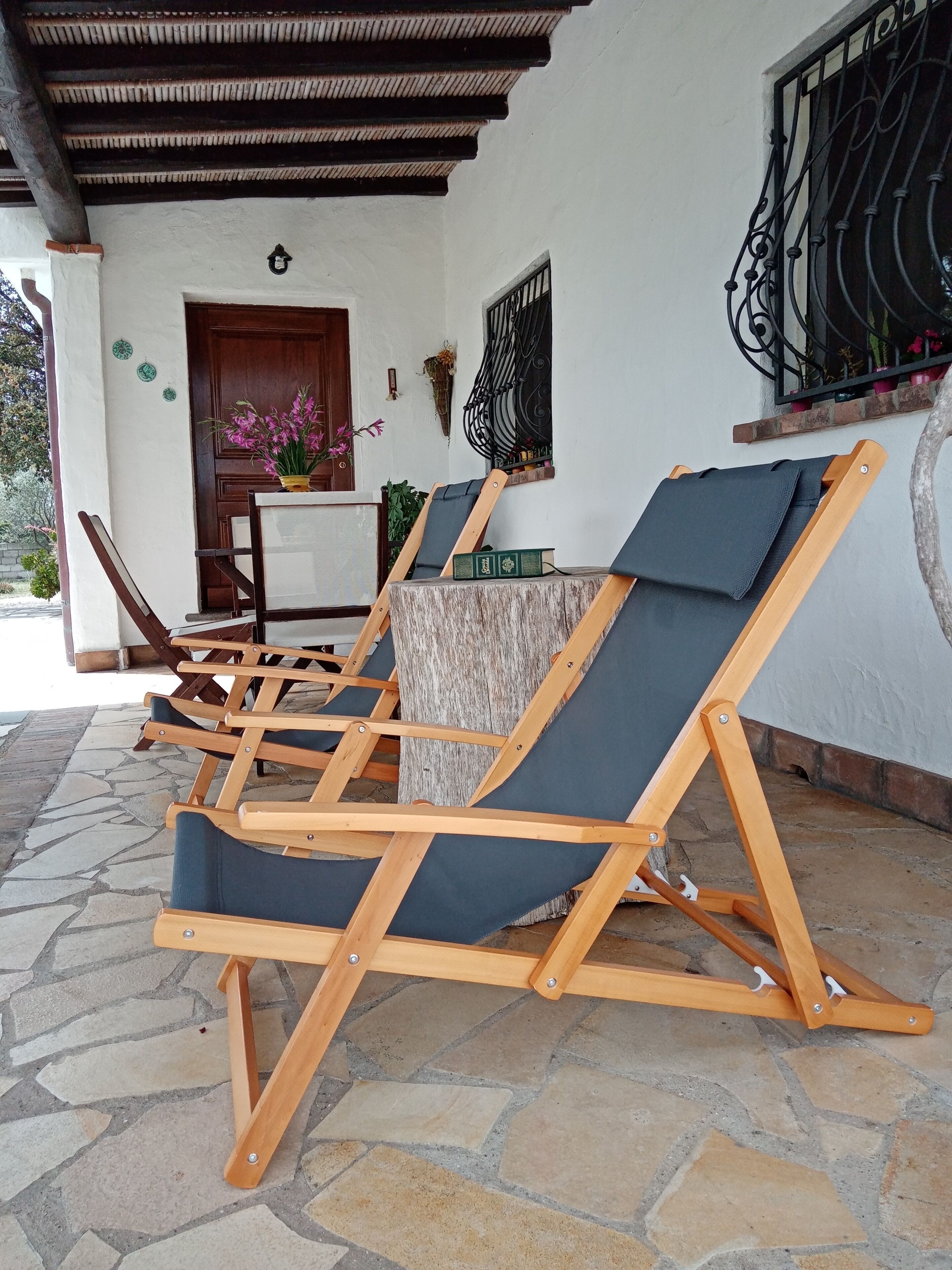 A covered outdoor seating area with wooden lounge chairs and a stone floor.