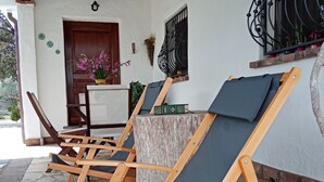 A covered outdoor seating area with wooden lounge chairs and a stone floor. - Villa Lupino (Orosei)