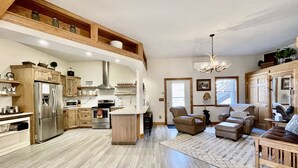 Une cuisine spacieuse équipée d’appareils modernes, un coin repas avec une table et des chaises en bois, et un salon avec un canapé et une cheminée.