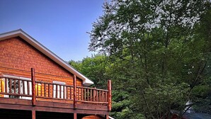 Une cabane en bois dotée d’un balcon, d’un foyer extérieur et de chaises Adirondack dans la cour.