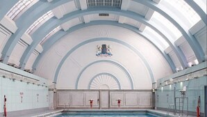 A large indoor swimming pool with a high arched ceiling and a central emblem. - Regent Style Soho Loft - Best of Both Worlds (London)