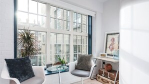 A bright room with large windows, two chairs, a small table, and a suitcase. - Regent Style Soho Loft - Best of Both Worlds (London)