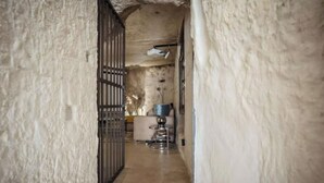 A narrow hallway with textured walls and a tiled floor leading to a room with a metal gate and a small table with a lamp.