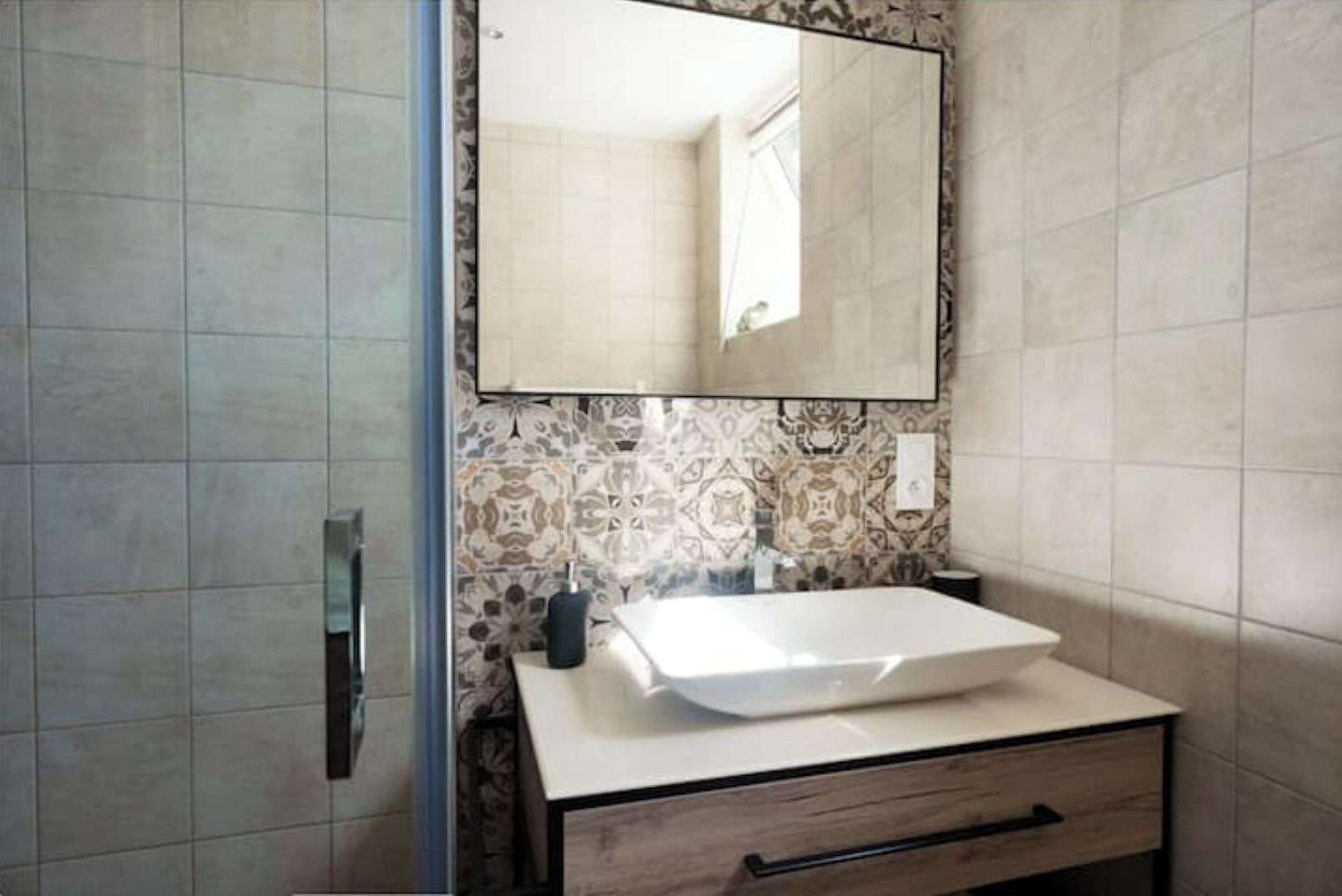 A bathroom with a white sink, a mirror, and patterned tiles on the wall.