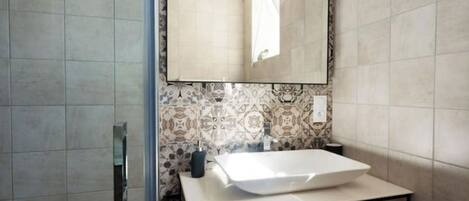 A bathroom with a white sink, a mirror, and patterned tiles on the wall.