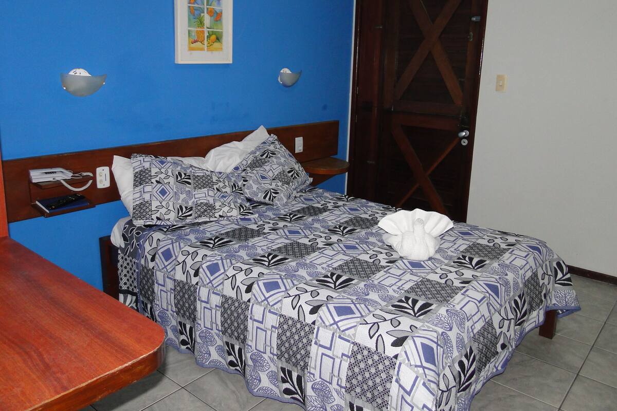 Una cama con una colcha estampada, un cabecero de madera y un teléfono montado en la pared.
