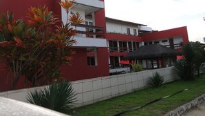 A modern building with a red facade, a balcony, and a thatched roof structure. - Pousada Lusitana (Ipojuca)
