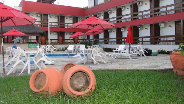 A hotel courtyard with a pool, lounge chairs, and red umbrellas. - Pousada Lusitana (Ipojuca)