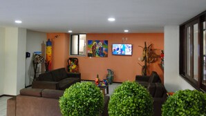 A living room with a sofa, a TV mounted on the wall, and a window. - Pousada Lusitana (Ipojuca)