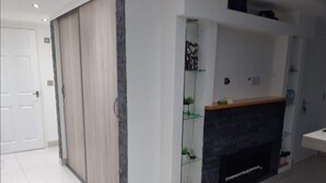 A modern living room with a fireplace, a white door, and a glass shelf with decorative items. - Lovely 2-bed Apartment in Coventry (Coventry)