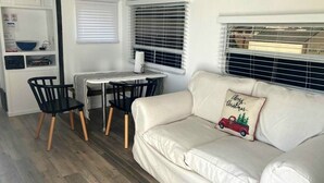 En ombonad inredning i husbilen med en vit soffa, ett matbord med stolar och ett köksområde med en spis och ett handfat.