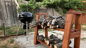 Ett träställ för ved och en svart grill med en skorsten.