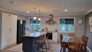 Une cuisine moderne dotée d’un îlot central, de luminaires suspendus, d’un four encastré et d’un coin repas avec des chaises et une table en bois.