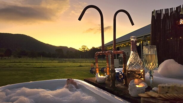 Un bain à remous dans un cadre extérieur rustique, comprenant une clôture en bois et une bouteille de vin.
