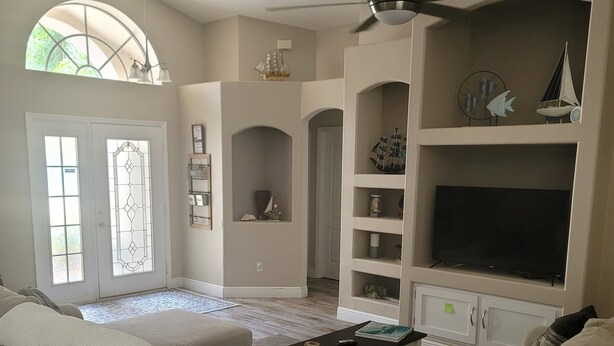 Una sala de estar con un sofá color beige, una mesa de centro, un televisor y objetos decorativos en estantes.