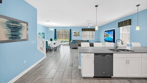 A modern kitchen with white cabinetry, a large island with a sink, and a dining area with a table and chairs. - 8BR Disney Getaway In Champions Gate! FREE POOL HEAT if you book by May 1st (Davenport)