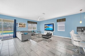 Relax in this stylish living room with a sofa, armchair, and flat-screen TV, offering a view of the outdoor pool.