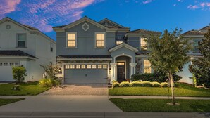 A two-story house with a front garage, a driveway, and a well-maintained lawn. - 8BR Disney Getaway In Champions Gate! FREE POOL HEAT if you book by May 1st (Davenport)