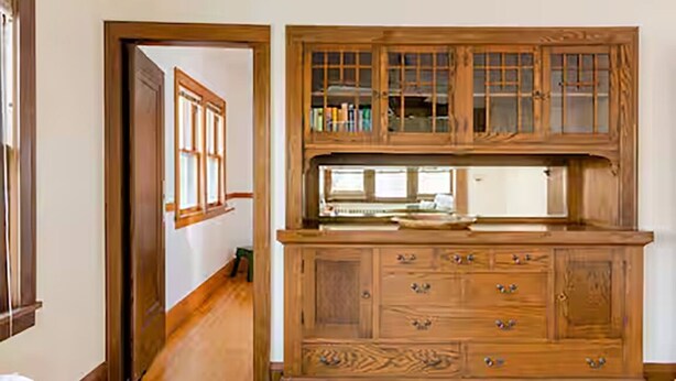 A wooden cabinet with multiple drawers and a glass top, placed in a hallway with wooden flooring and a door on the left. - Classic Macalester Area St. Paul Duplex (Saint Paul)