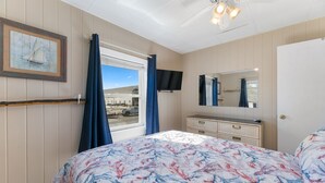 A bedroom with a bed, a dresser, a television, and a window with curtains.