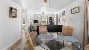 A dining area with a glass table, wicker chairs, and a ceiling fan.