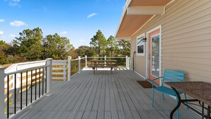 A wooden deck with a white railing, a picnic table, and a blue chair.