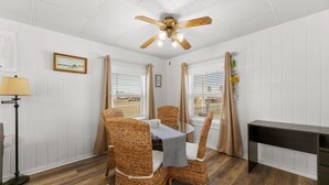 A dining area with wicker chairs, a round table, a ceiling fan, and a view of the outside through windows.