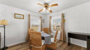 A dining area with wicker chairs, a round table, a ceiling fan, and a view of the outside through windows.