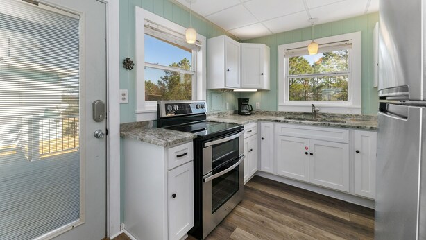 A kitchen with white cabinets, a stainless steel refrigerator, a double oven, and a granite countertop.