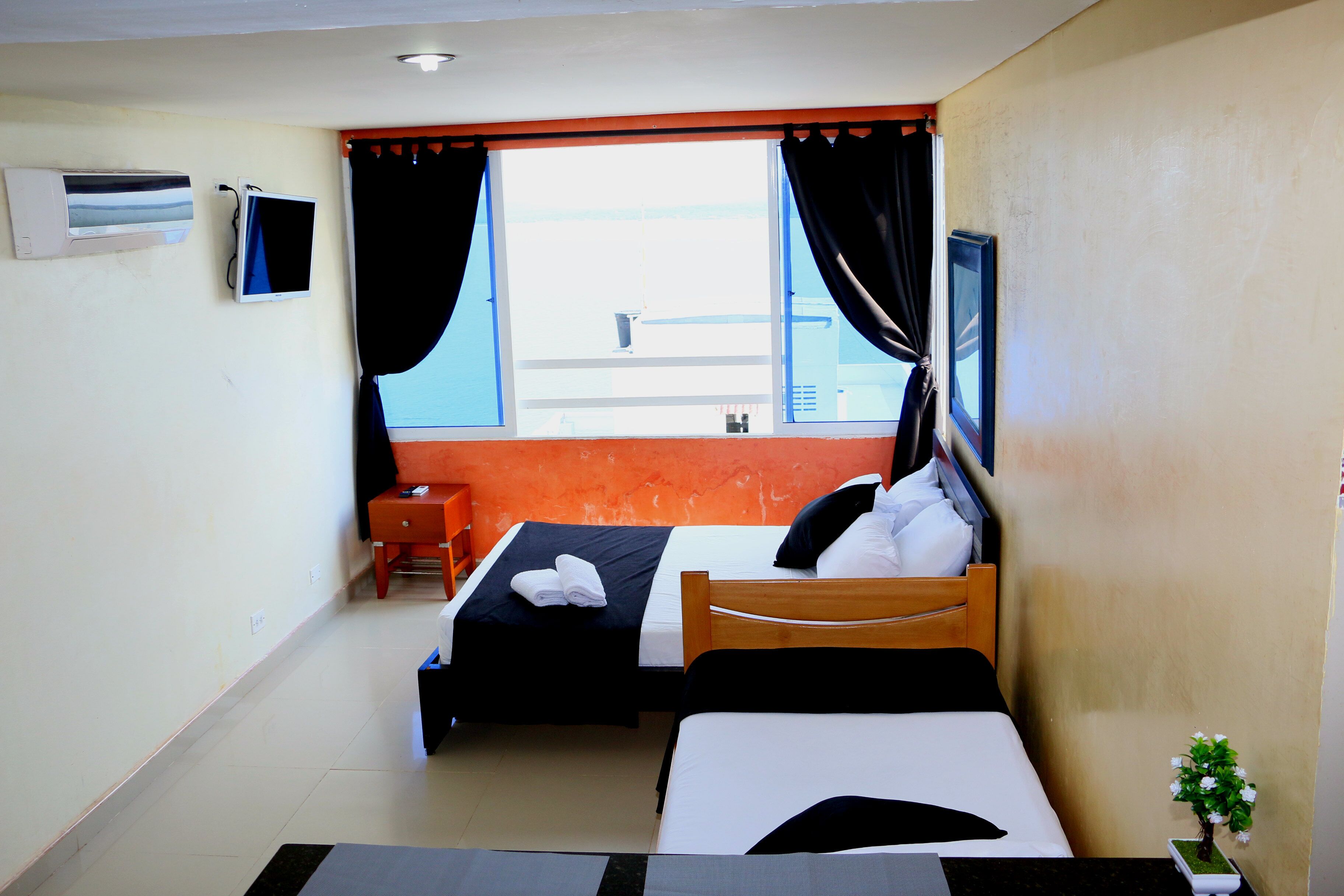 Une chambre d’hôtel avec deux lits, une petite table, un climatiseur, une télévision et une fenêtre avec des rideaux.