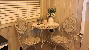 A cozy room with wooden walls, a window with blinds, a small round table with two chairs, and a vase with flowers. - Cozy Historic Cabin Near Hiking (Wolf Creek)