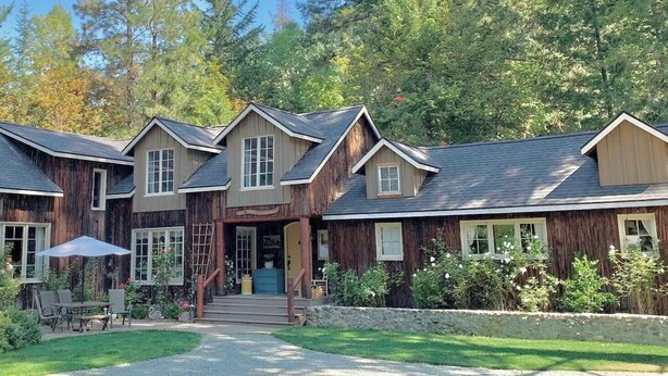 A rustic lodge with a central entrance, multiple windows, and a stone pathway leading to a seating area. - Cozy Historic Cabin Near Hiking (Wolf Creek)