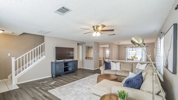 A spacious living room with a wooden floor, a beige sofa, a coffee table, and a ceiling fan. - Fresh, Clean & Comfortable Place in Round Rock (Round Rock)