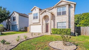 A two-story house with a garage, a front entrance, and a landscaped front yard with a small tree and shrubs. - Fresh, Clean & Comfortable Place in Round Rock (Round Rock)