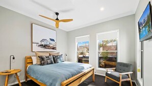 Une chambre à coucher moderne avec un lit en bois, un ventilateur de plafond, un bureau et une chaise.
