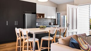 Une cuisine moderne dotée d’un îlot central, de meubles de couleur sombre et d’un coin repas avec des chaises blanches.