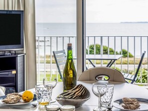 A dining table with a bottle of wine, glasses, and plates of food, set against a view of the sea. - Les Trois Iles by Interhome (Quiberon)