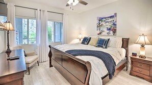 Ein Schlafzimmer mit Bett, Nachttischen, Schreibtisch, Stuhl, Deckenventilator und einem Fenster mit Vorhängen.