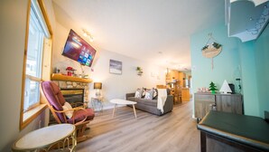 Een woonkamer met een open haard, een aan de muur bevestigde televisie en een eethoek met een tafel en stoelen.