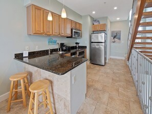 A kitchen with wooden cabinets, granite countertops, stainless steel appliances, and a small island with stools.