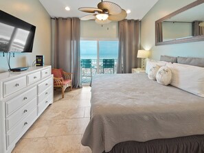 A hotel room with a bed, a TV, a dresser, a chair, and a balcony with a view.