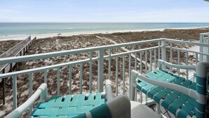 En balkon med udsigt over stranden, en træbro og strandstole.