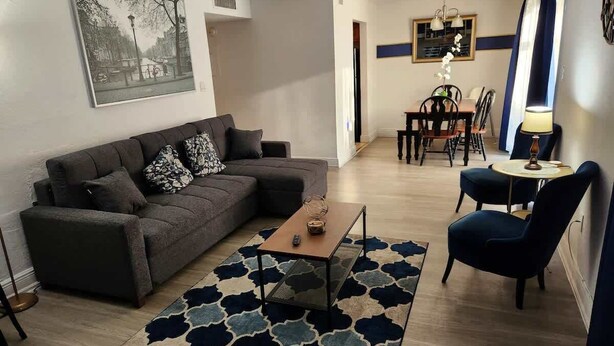 A living room with a sofa, coffee table, rug, and a dining area with chairs and a table. - Near Universal and other Orlando Attractions (Orlando)