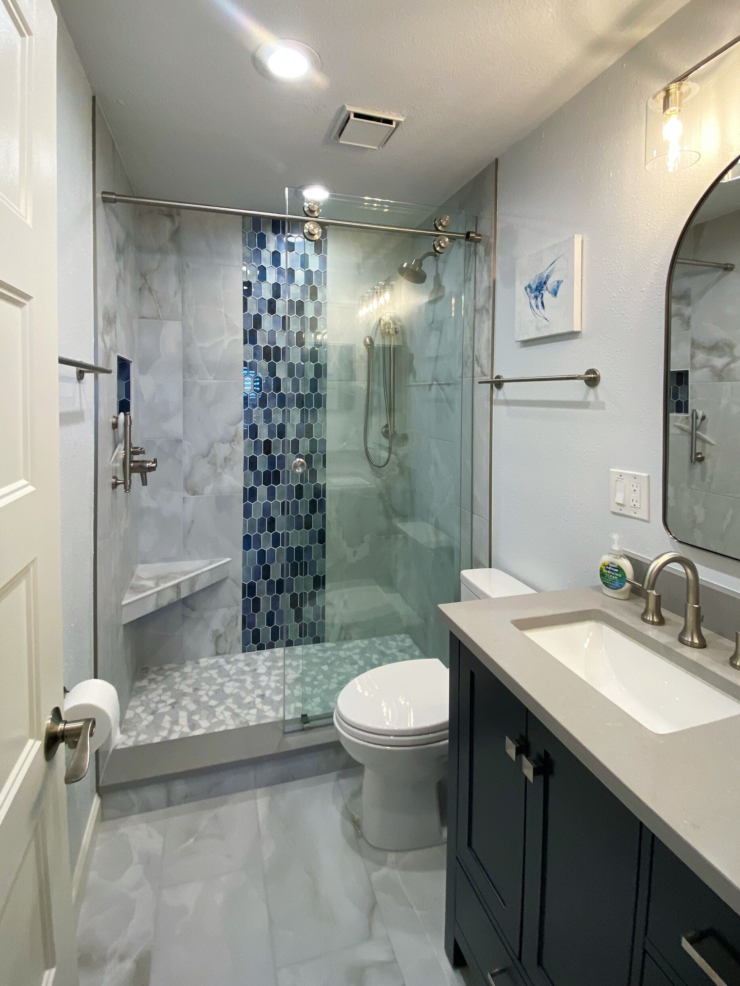 Un baño moderno con ducha de vidrio, inodoro blanco y tocador con lavamanos y espejo.